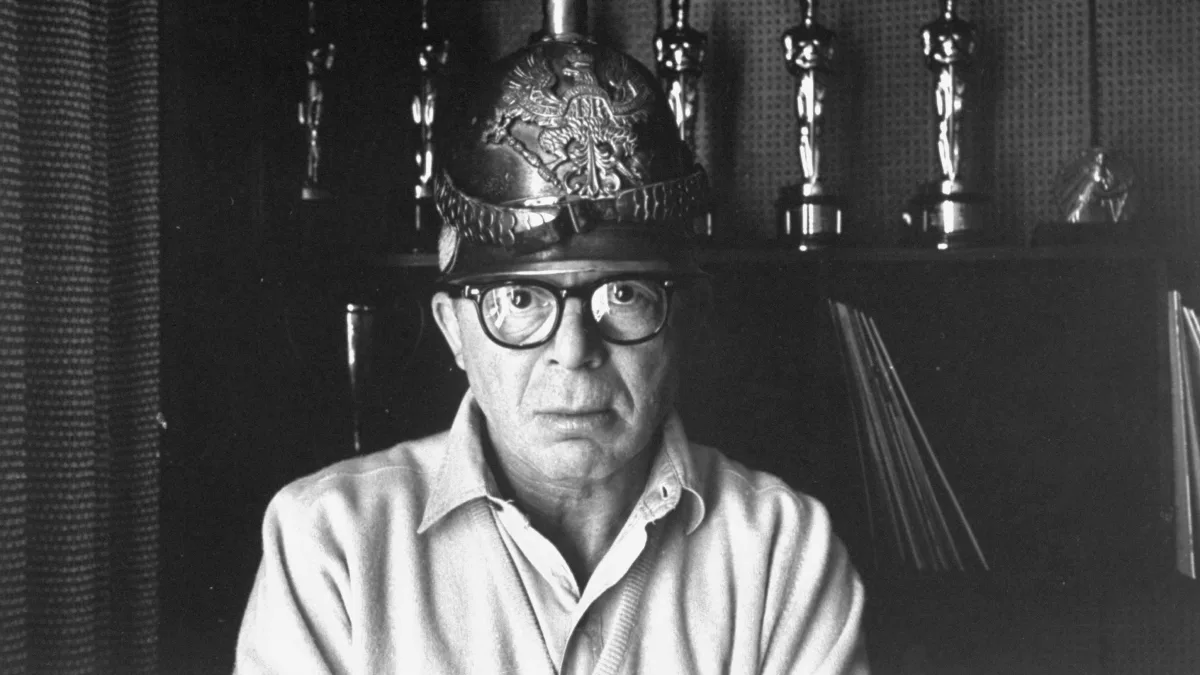Director  Billy  Wilder  in  his  Hollywood  office  wearing  German  helmet  w.  Oscars  on  shelf