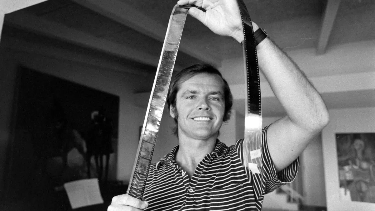 American  film  actor  Jack  Nicholson  grims  as  he  holds  up  a  strip  of  film  negative  in