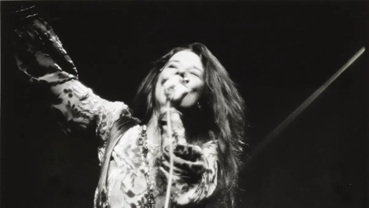 Janis Joplin on stage at New York City's Madison Square Garden, holding a microphone in one hand the