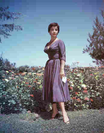 Full-length portrait of British-born actor Elizabeth Taylor as she stands in a garden and holds a handkerchief in her right hand, circa 1950s.