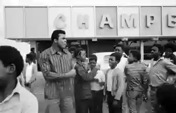 Professional  boxer  Muhammad  Ali  standing  with  a  group  of  children  near  a  grocery  store