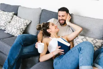 Content ethnic couple sitting on sofa together while looking at each other and relaxing at weekend at home, Model releas
