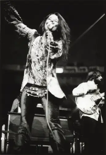Janis Joplin on stage at New York City's Madison Square Garden, holding a microphone in one hand the