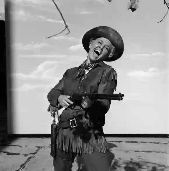 American  actress  and  singer  Doris  Day,  in  a  buckskin  cowgirl  costume,  aims  a  rifle  in