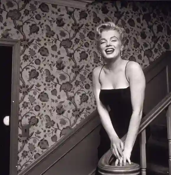 Marilyn Monroe (1926 - 1962) stands in a staircase alongside a wall with a floral-motif pattern, late 1950s.
