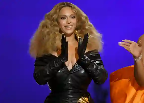 Beyoncé claps her hands, which she's wearing black gloves on
