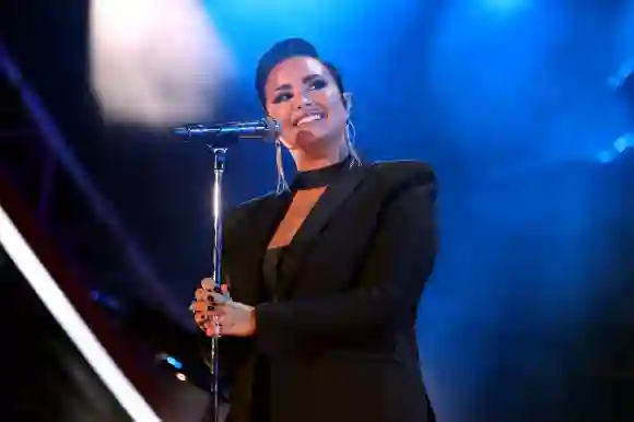 Demi Lovato stands on stage, smiles and holds her microphone in both hands