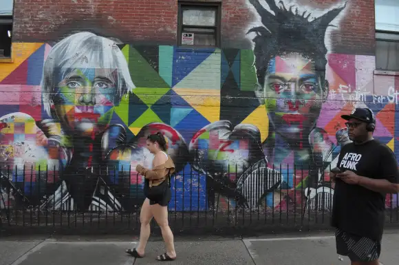 August 26, 2024, New York, United States: A woman walks past a wall painting of Andy Warhol and Jean-Michel Basquiat in