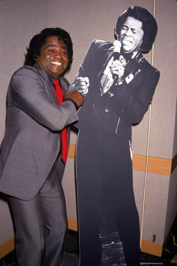 American    rhythm  and  blues,  soul,  and  funk  musician  James  Brown  poses  next  to  a  cardb