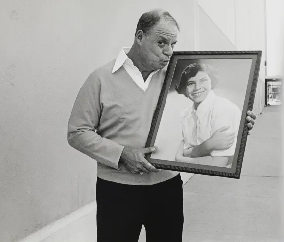 American  comedian  Don  Rickles,  holds  and  kisses  a  framed  picture  of  his  wife,  as  a  yo
