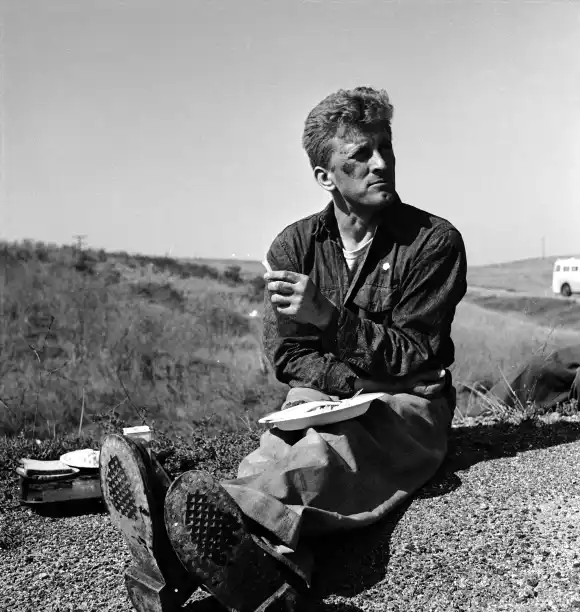 American  actor  Kirk  Douglas  sits  by  the  side  of  a  road  and  eats  lunch  on  the  set  of